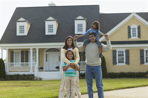 A family of four standing in front of a yellow house 